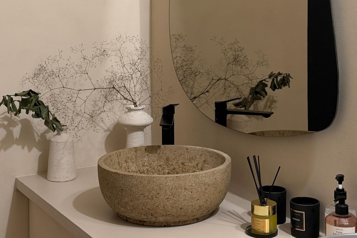 Organic minimalist microcement bathroom with stone vessel sink, asymmetric mirror, dried botanicals and matte black hardware