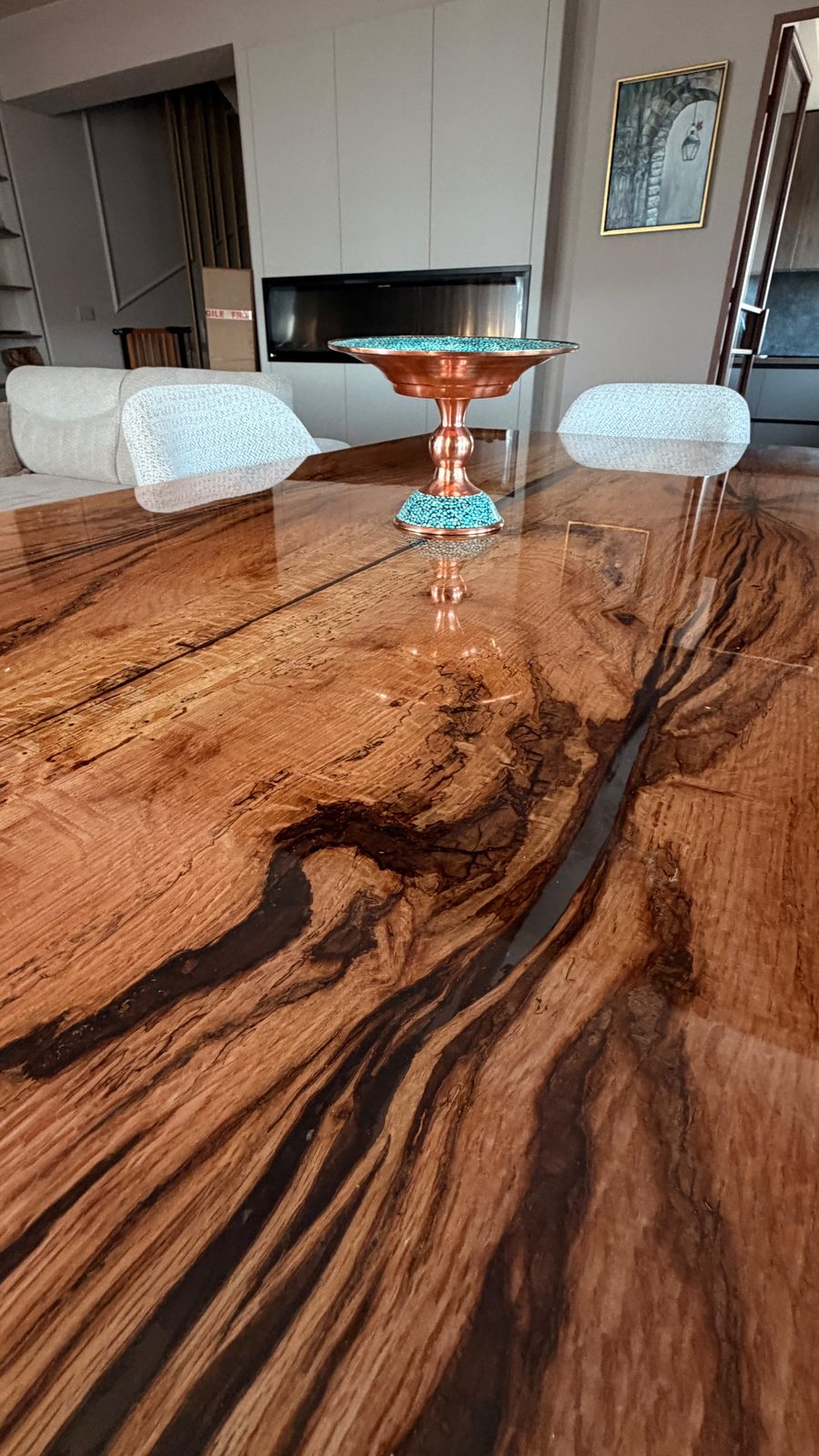 Close-up of oak grain with dark mineral streaks and a thin line of translucent resin filling a natural crack under a glossy epoxy surface